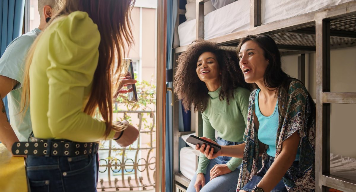Women students talking about a social network content on the smartphone screen sitting on bunk bed of an hostel room