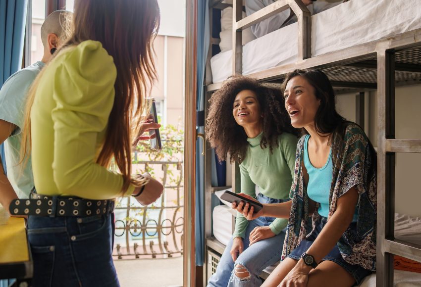 Women students talking about a social network content on the smartphone screen sitting on bunk bed of an hostel room